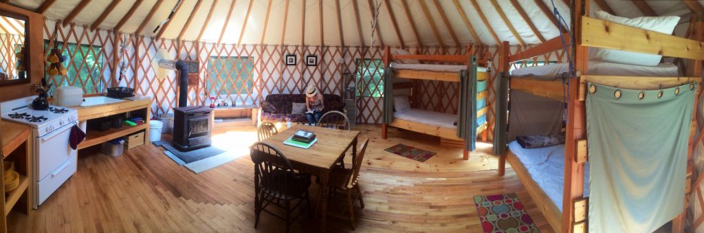 the interior of a glamping yurt with a kitchen, bunk beds, and a dining table 