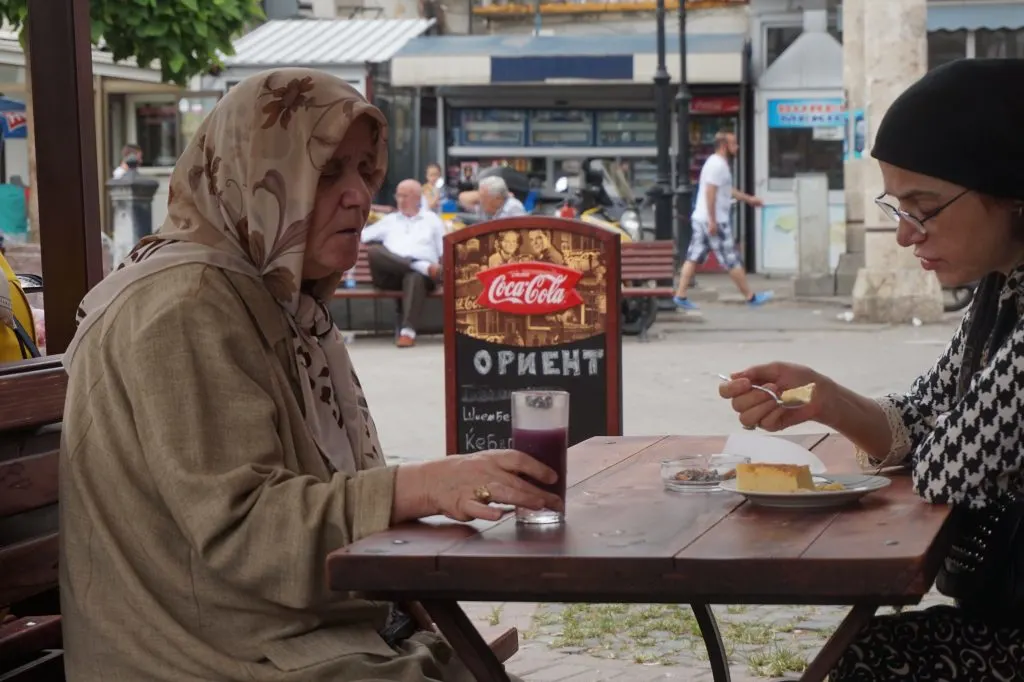 Two Muslim women wearing headscarves sitting at a table, eating dessert and drinking juice