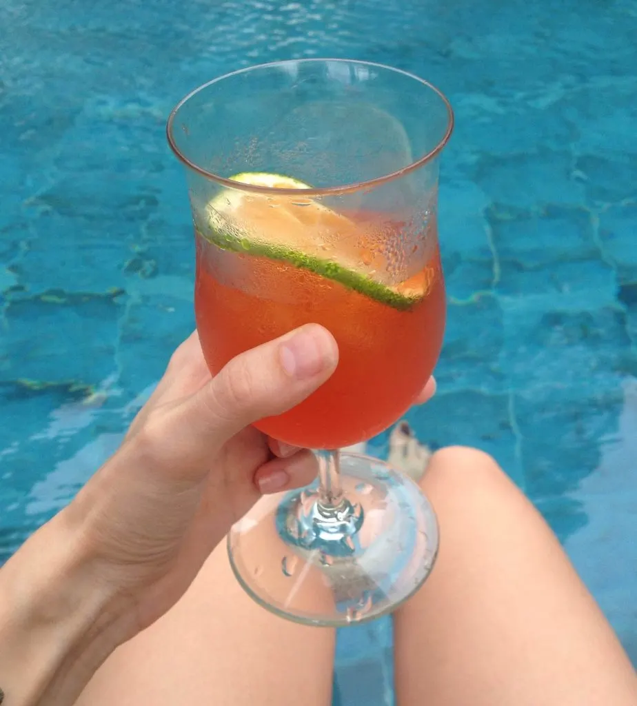 a woman's hand holding a cocktail glass over a pool