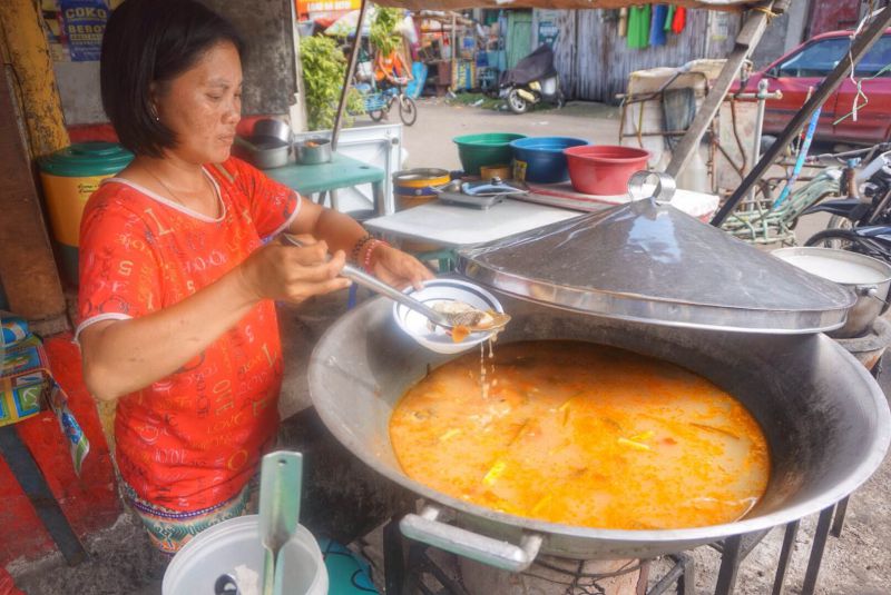 A Philippine woman serving a soup dish from a massive pot on the street into a plate