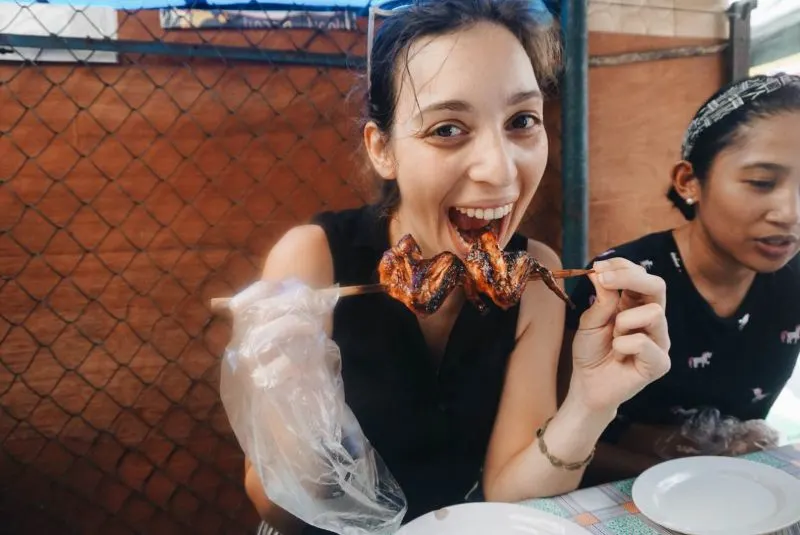 A woman biting into a meat skewer in Philippines