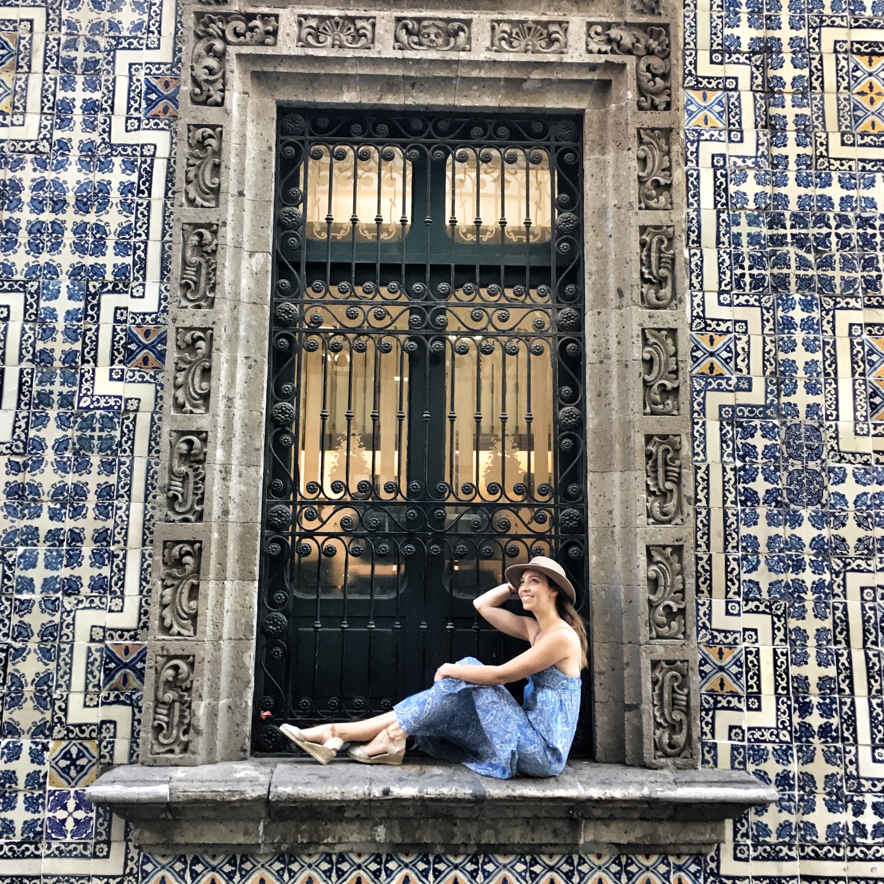 A woman sitting on a window sill surrounded by blue and white tiles