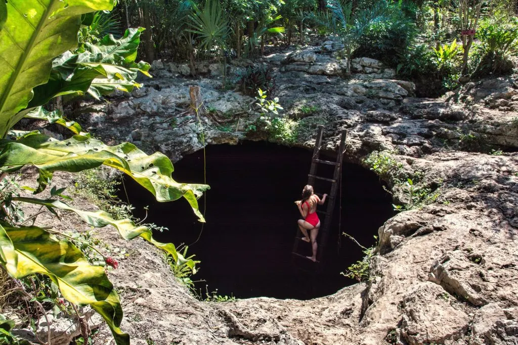 A woman standing in a wooden ladder at the entrance of an underground cenote