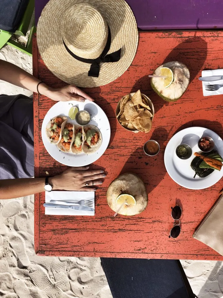 An overhead shot of a plate with tacos, a bowl of chips, and a coconut drink on a table