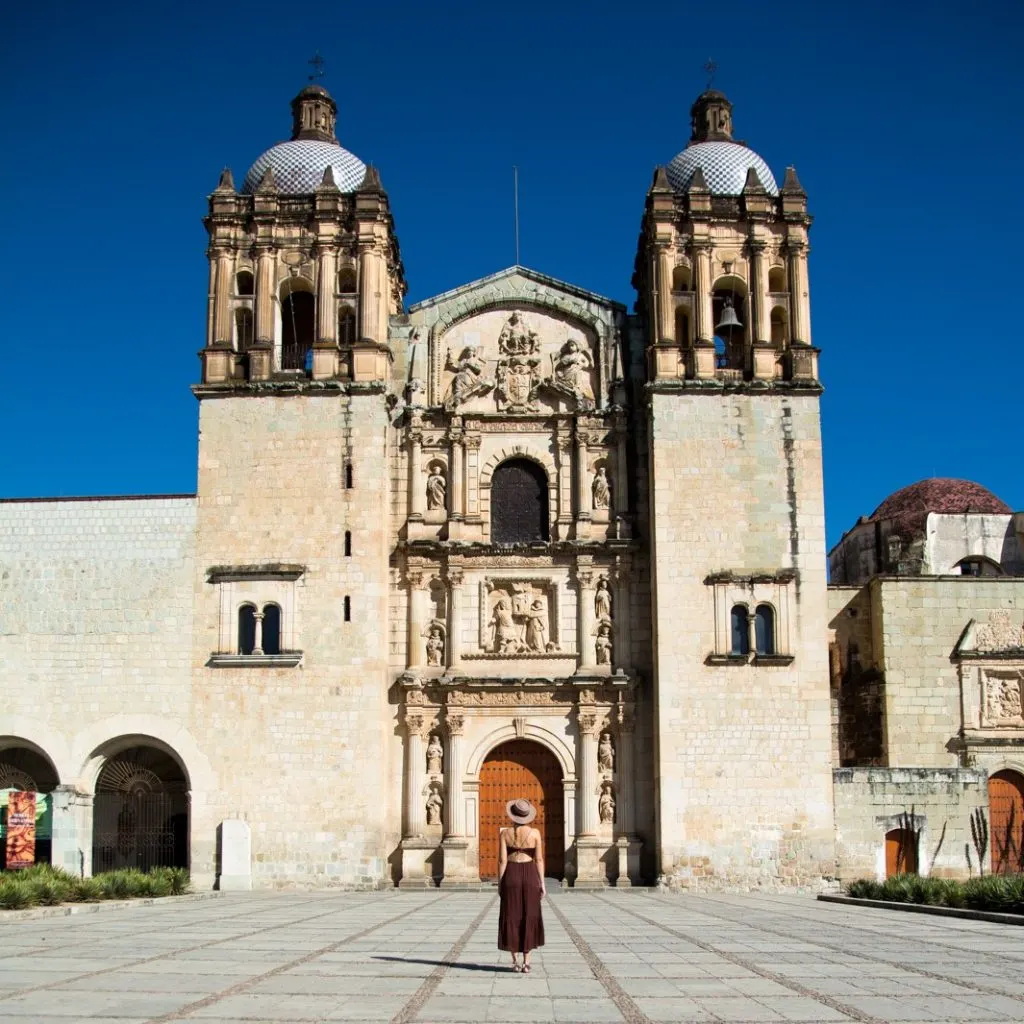 A woman standing in front of a large church, the Templo de Santo Domingo in Oaxaca's historic center, one of the Unesco World Heritage Sites in Mexico.  