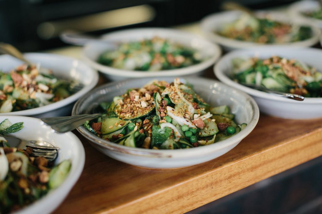 several bowls with a green salad topped with nuts