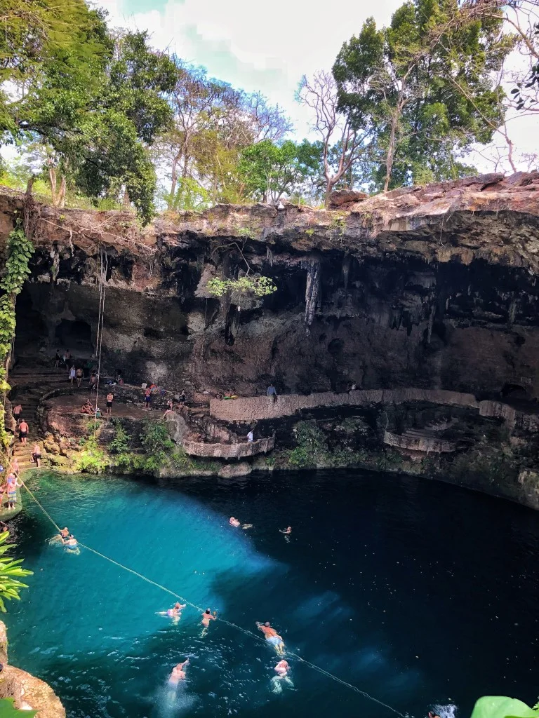 People swimming in cenote zaci, with a large rock wall on the side of the cenote