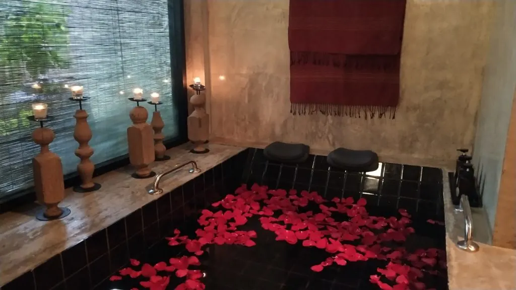 A tub with rose petals floating in the water, and candles