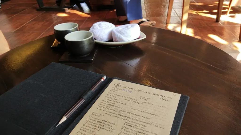 A spa consultation card on a table, with two bowls of tea and rolled towels in the background