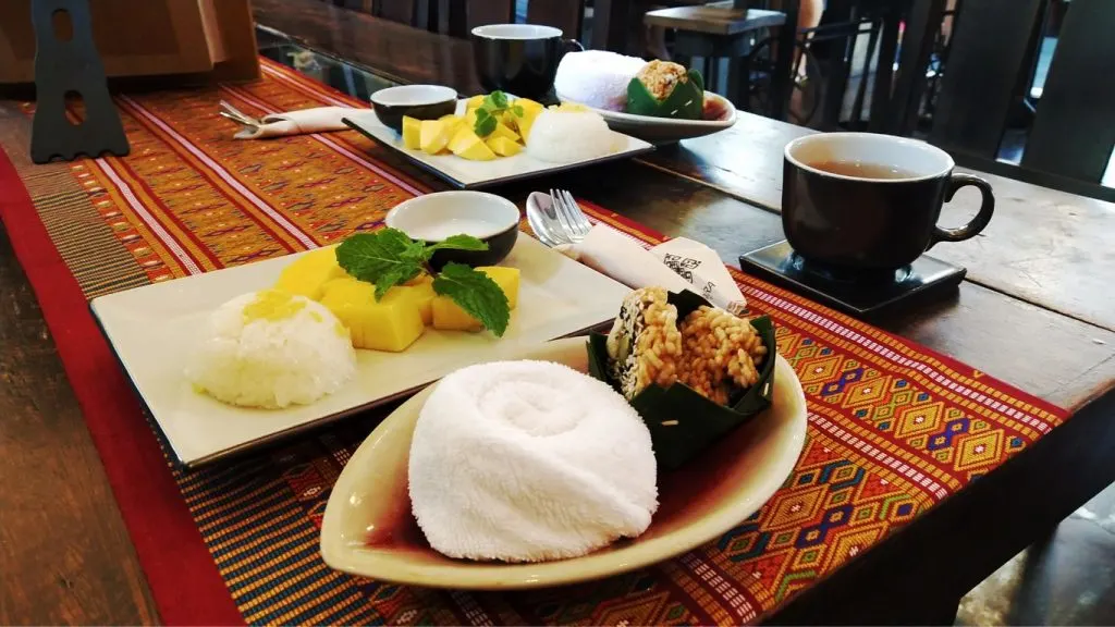 Two plates with mango sticky rice and cups of tea in a table