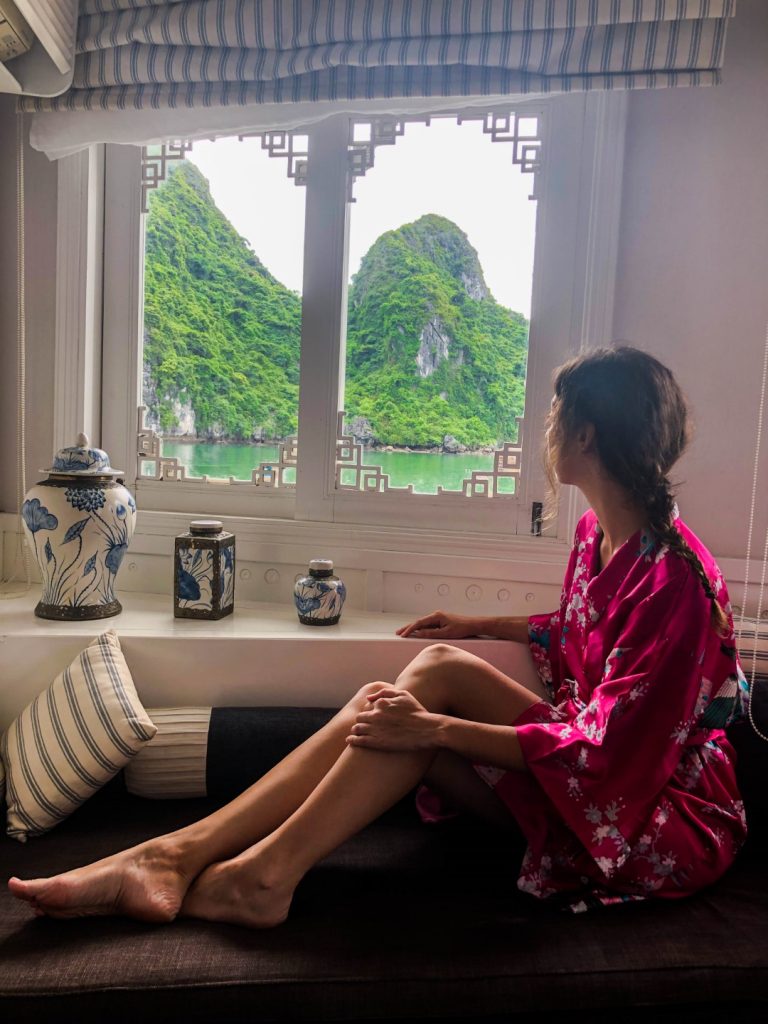 A woman in a pink silk robe looking out the window at the impressive karsts of Halong Bay