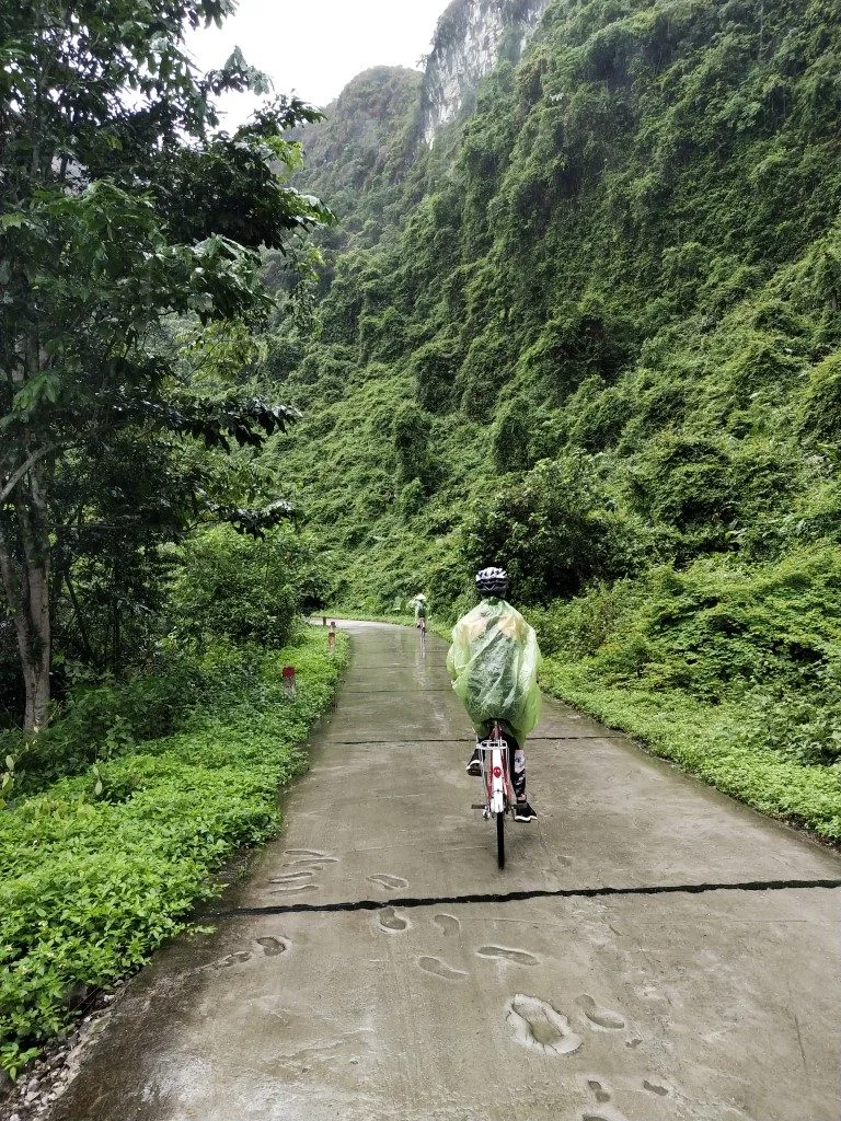 A woman riding a bicycle wearing a helmet and a green poncho