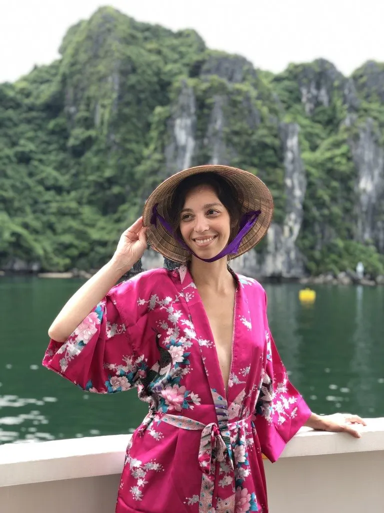 A woman wearing a Vietnamese hat and a silk robe posing in front of massive karsts 