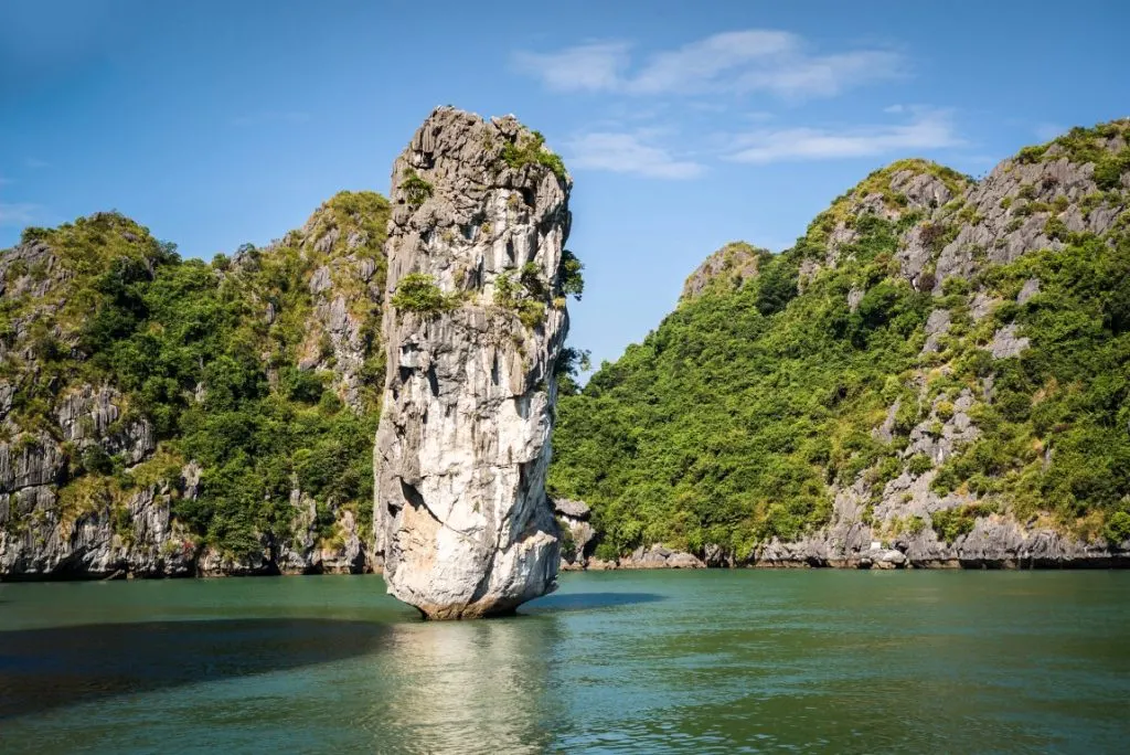 A single karst emerging from the water in Halong Bay, with massive other ones in the background