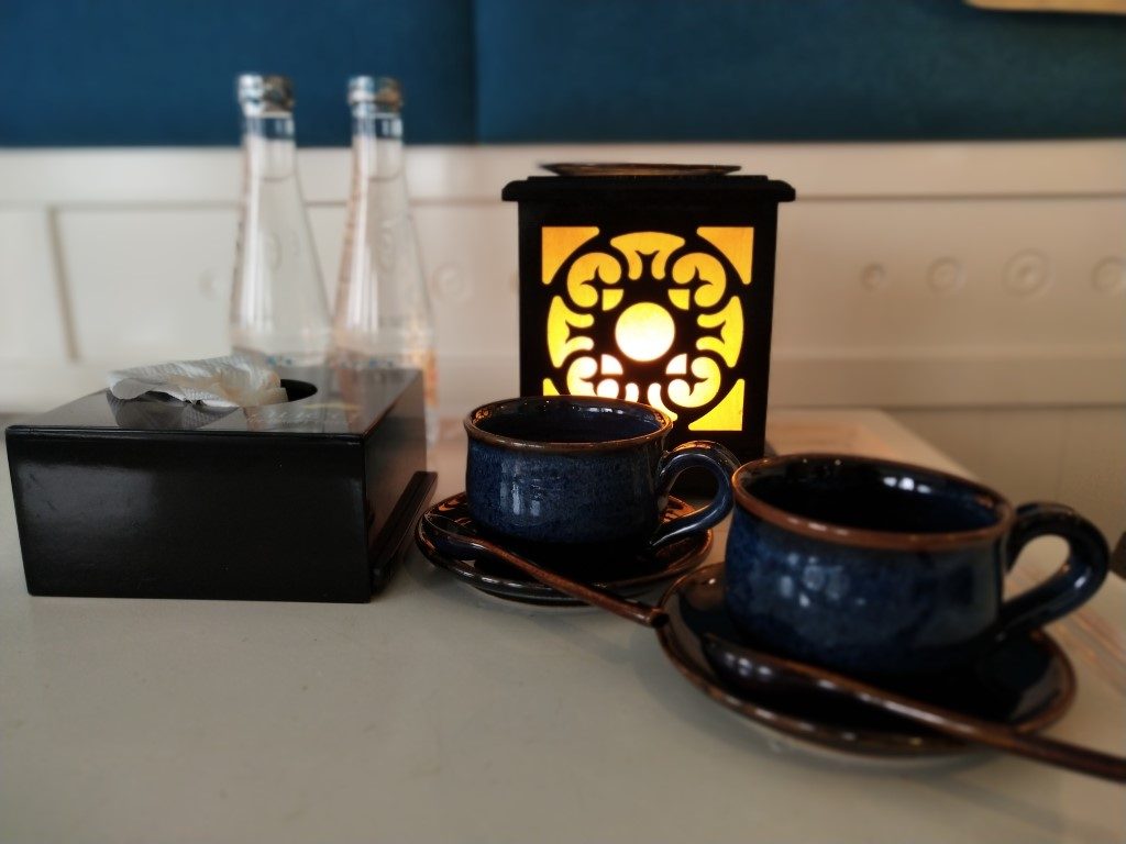 Two coffee mugs on a table, with a lamp and a box of tissues on the side