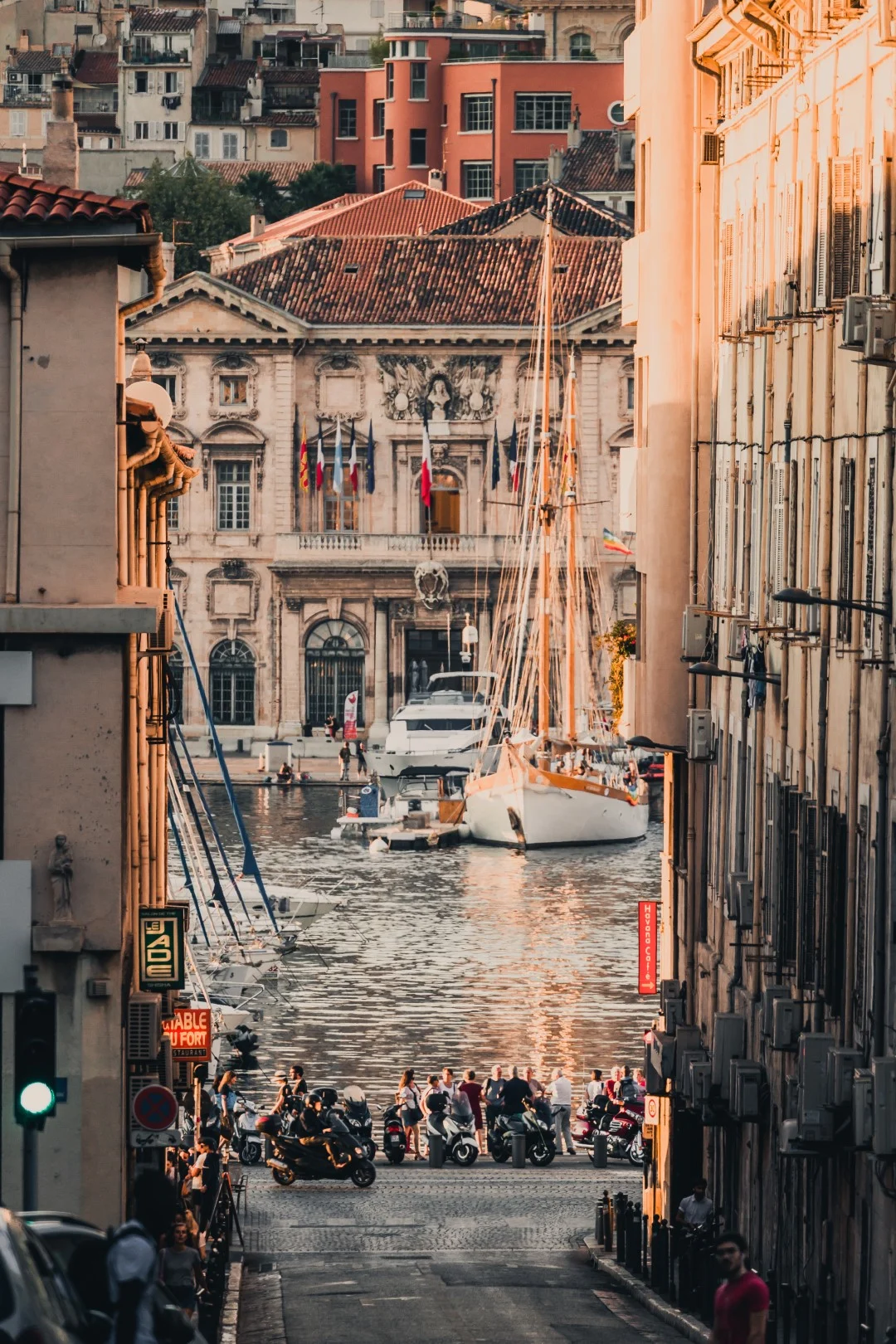 An image of Marseille, with a boat in a canal, motorbikes parked by the lake, and a grand building on the other side of the water