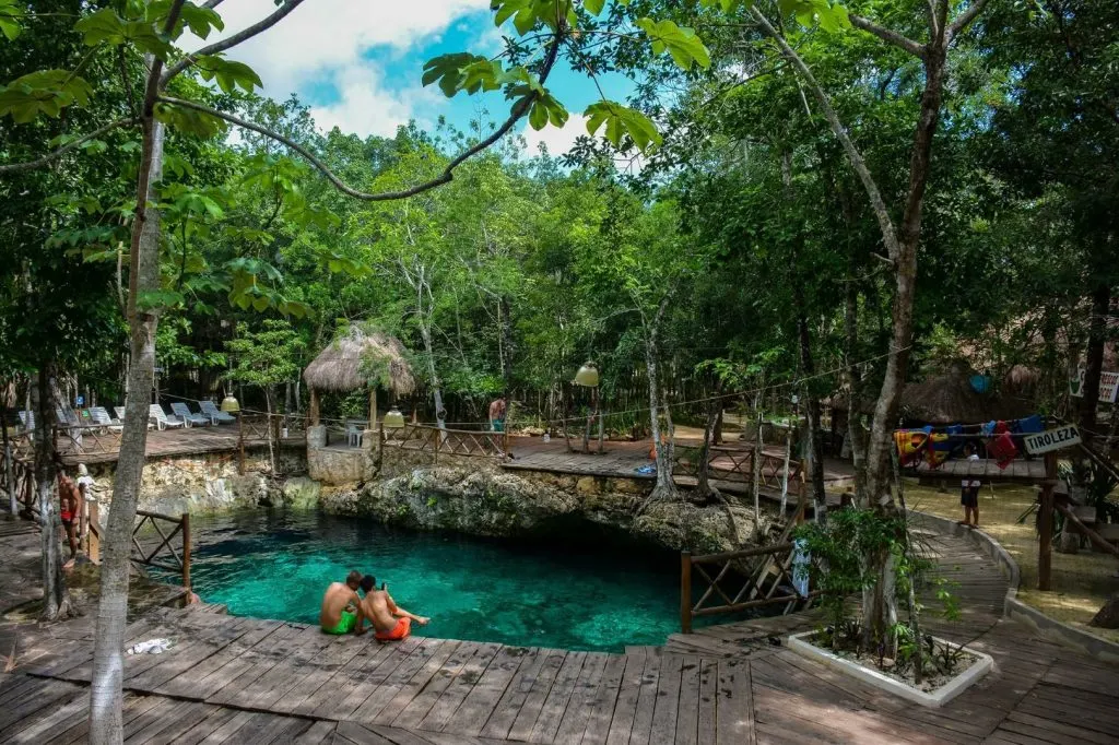 An image of Zacil Ha Cenote, with two kids sitting on the edge of the water 