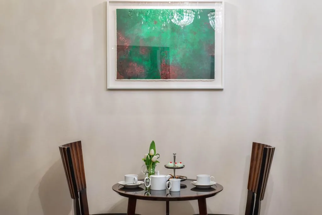 Image of a breakfast table with two chairs, and a green painting hanging on 
 a white wall 