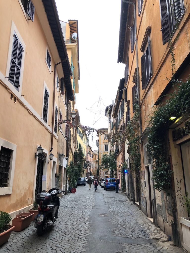 A narrow cobblestone street in Rome, with a motorbike parked on the side