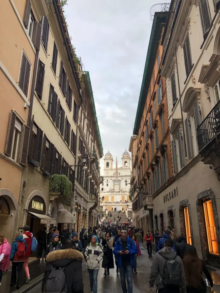 Via Condotti facing the Spanish Steps in Rome, with a large crowd walking along 