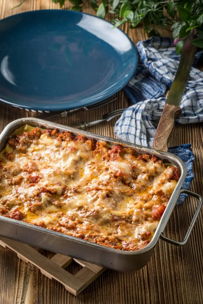 A lasagna dish and a blue plate in the background, inserted in a post about the best Bologna restaurants