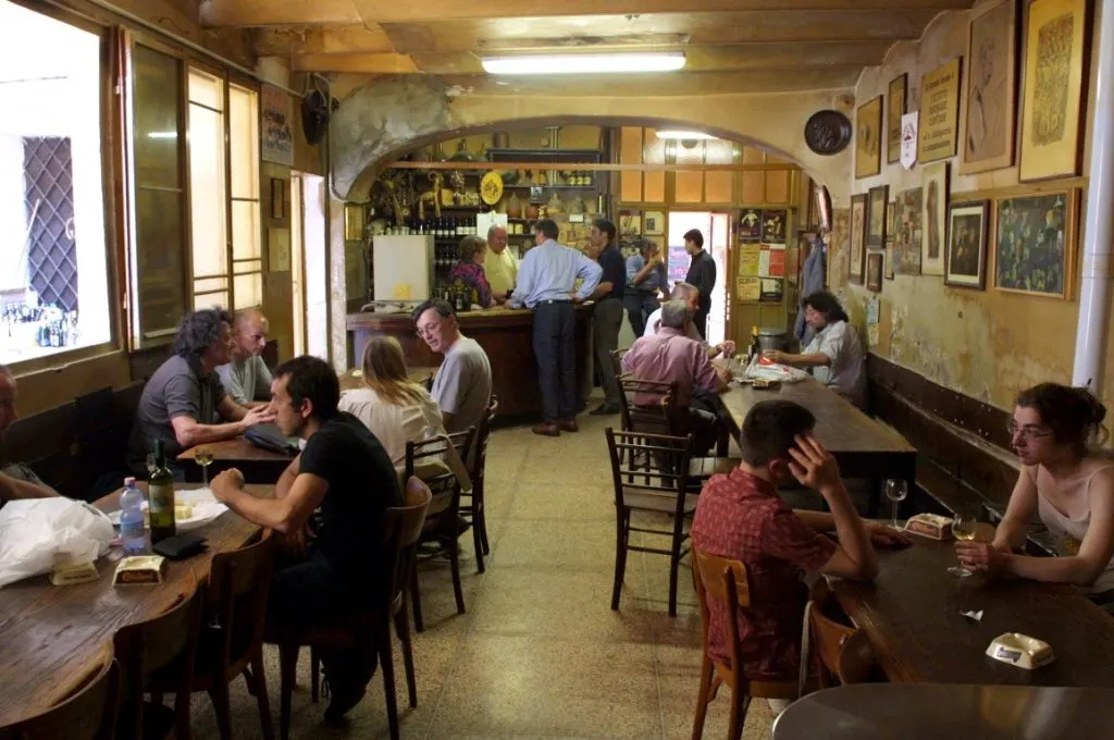 An Italian osteria with wooden tables, a bar, and people enjoying a drink 