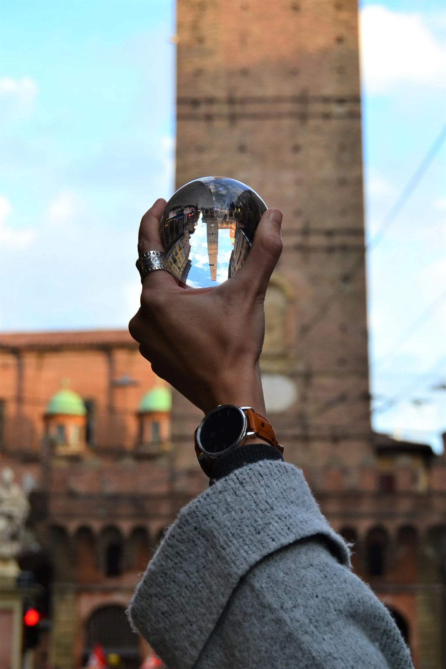 A hand holding a glass sphere in front of Torre degli Asinelli in Bologna 