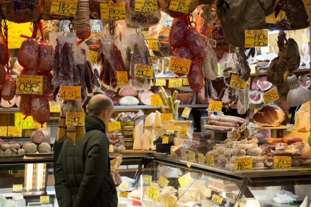 A man standing in front of a cheese and cured meats shop in Quadrilatero, Bologna 