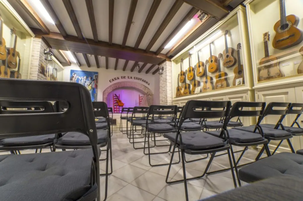 A flamenco center with a small stage in the back, black chairs for the public, and guitars on the walls