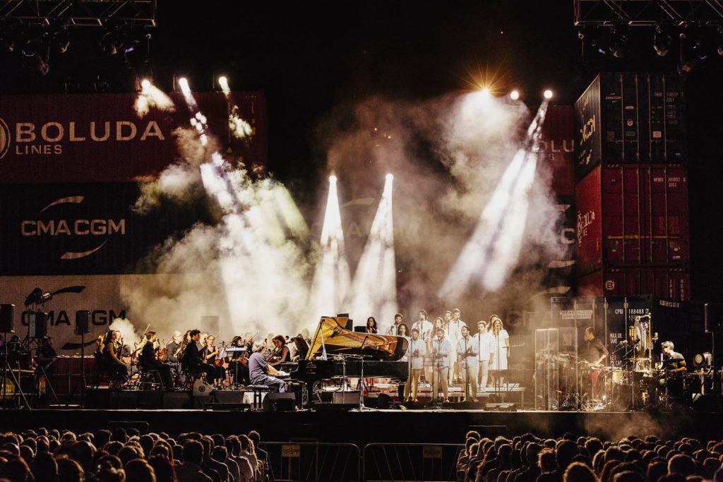 A large stage with an orchestra and a chorus, and the audience sitting in the forefront of the image