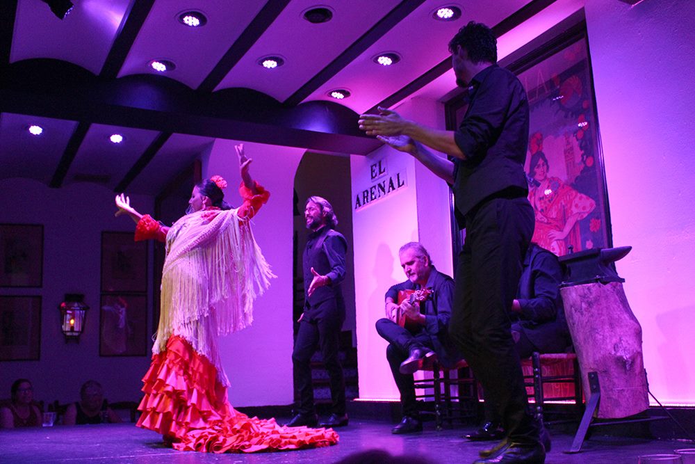 A couple of flamenco dancers performing on stage, with a singer and a guitar player in the back 