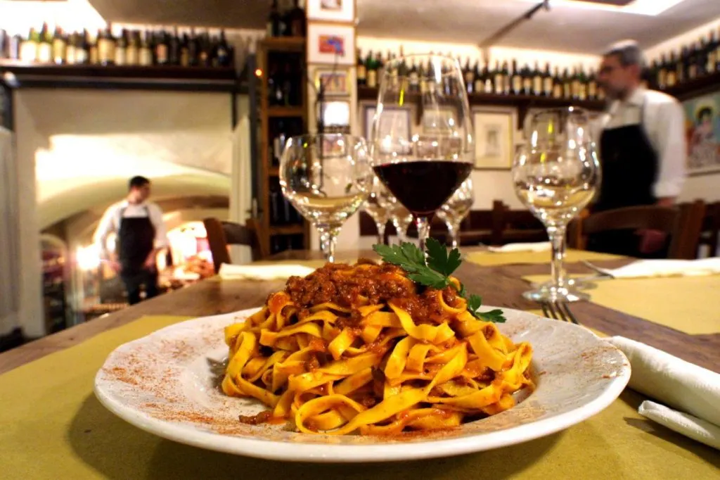 A dish of handmade pasta with ragú sauce, and a glass of red wine in a trattoria 