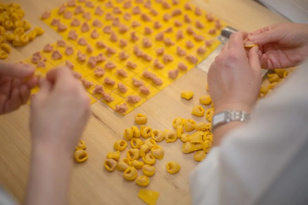 Two pairs of hands handmaking tortellini