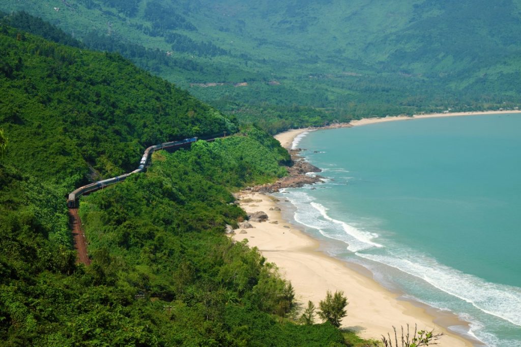 A long stretch of beach with blue sea, backed by lush green mountains