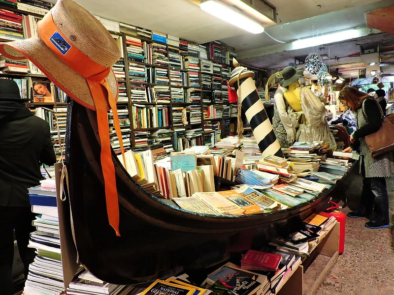 A packed bookshop in Venice, with a gondola brimming with books and visitors browsing 