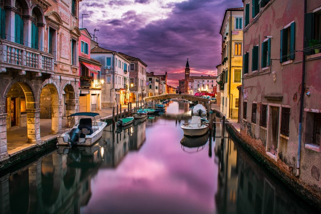 A peaceful Venetian canal, lined with old buildings under a purple sky 