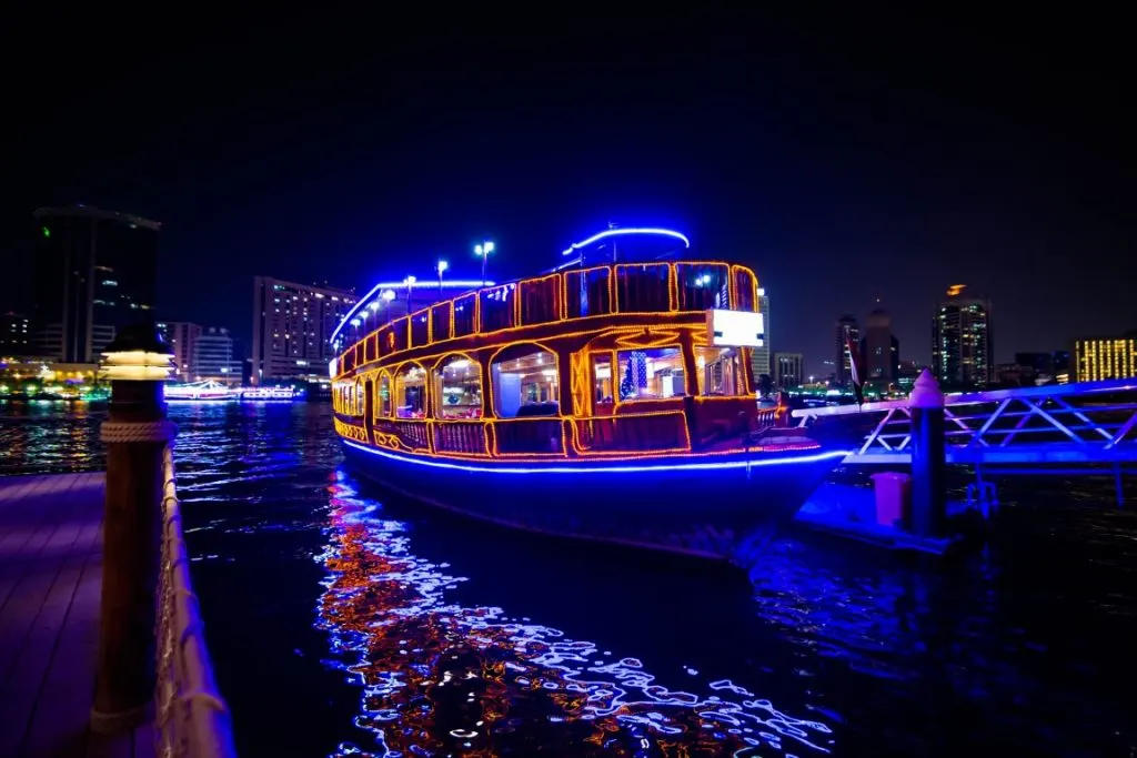 A dhow cruise in the water at night, with blue and orange lights