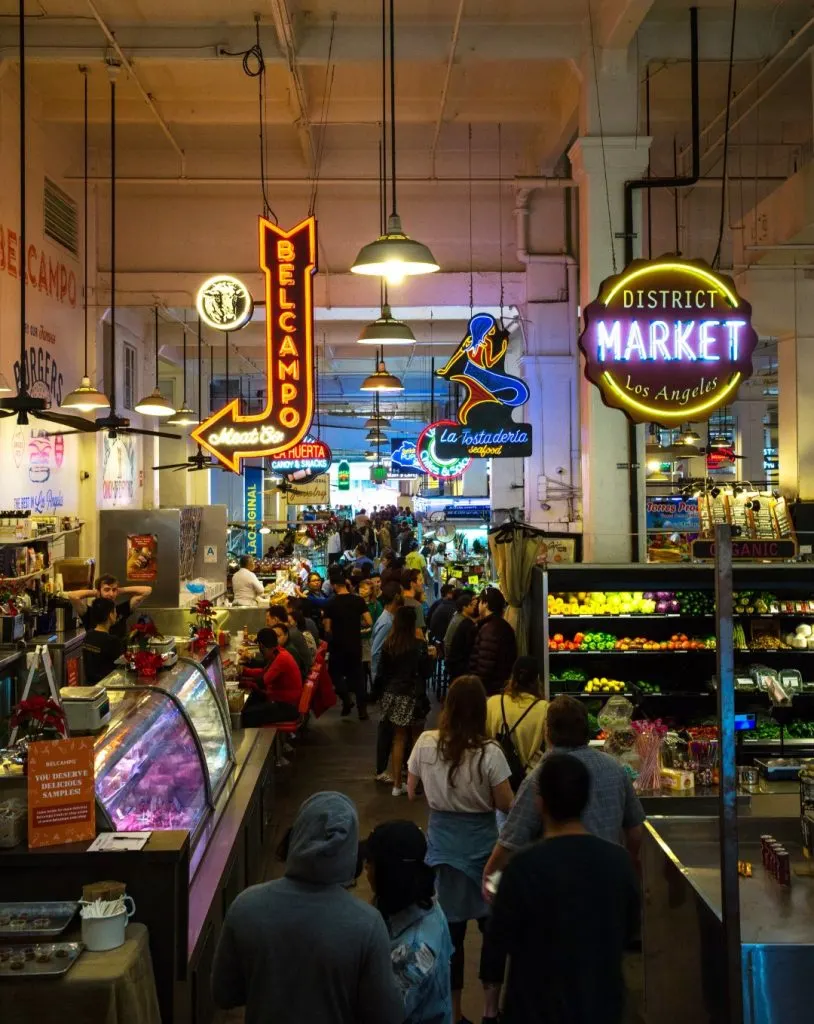 the bustling interior of a food market with stalls, seating areas, and neon signs