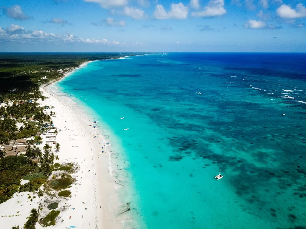 An overview image of a beach in the Caribbean Sea, with the turquoise sea on the right, a long stretch of white sand, and jungle on the left