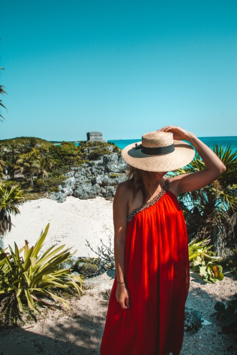 A woman in a red dress posing in front of the Tulum ruins