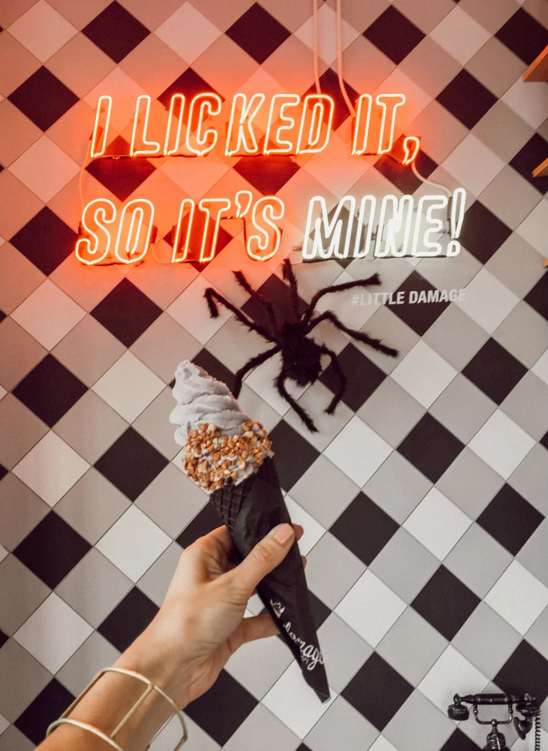 A woman's hand holding an ice cream in a black cone in front of a neon sign that reads ''I liked it, so it's mine''