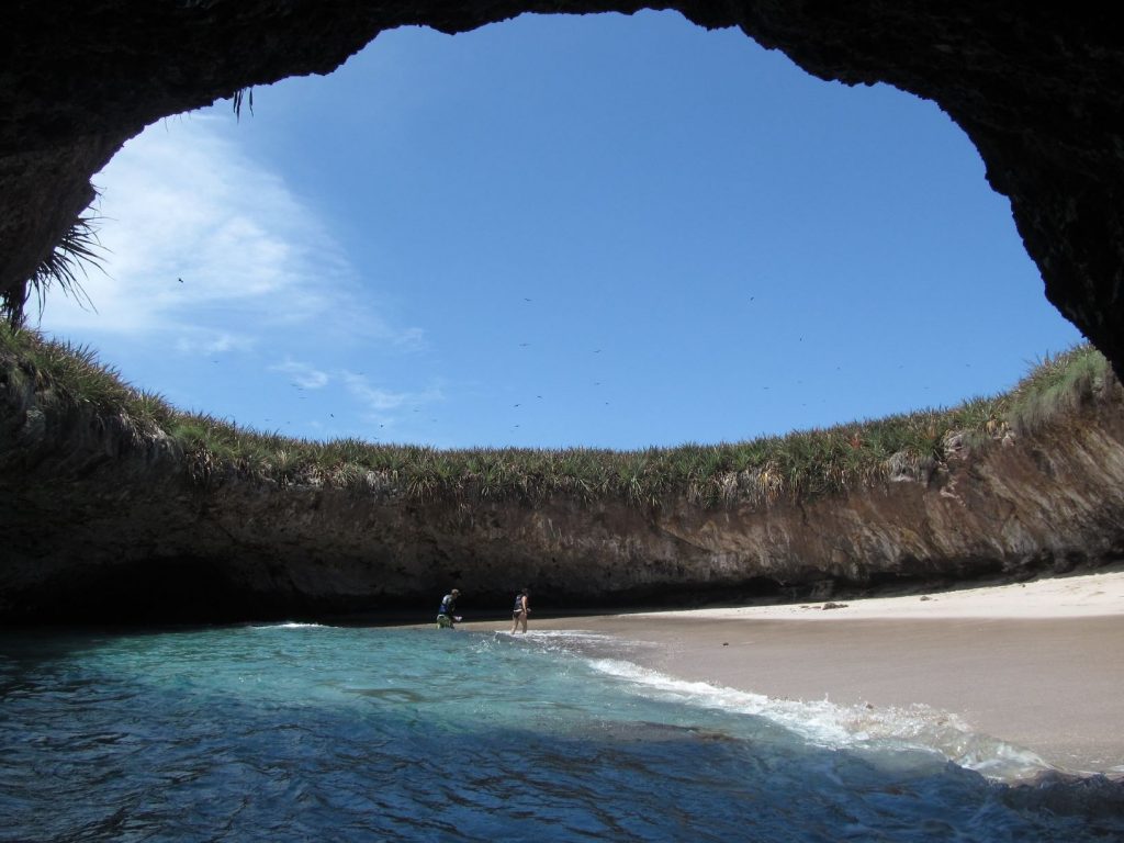 A beach inside a cave with a grand circular opening to the sky