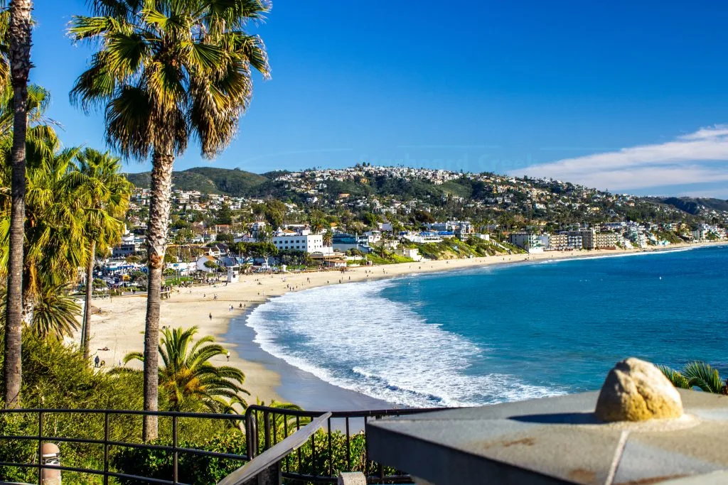 An image of Laguna Beach, showcasing the blue sea on the right, and the coastline with houses and vegetation on the left 