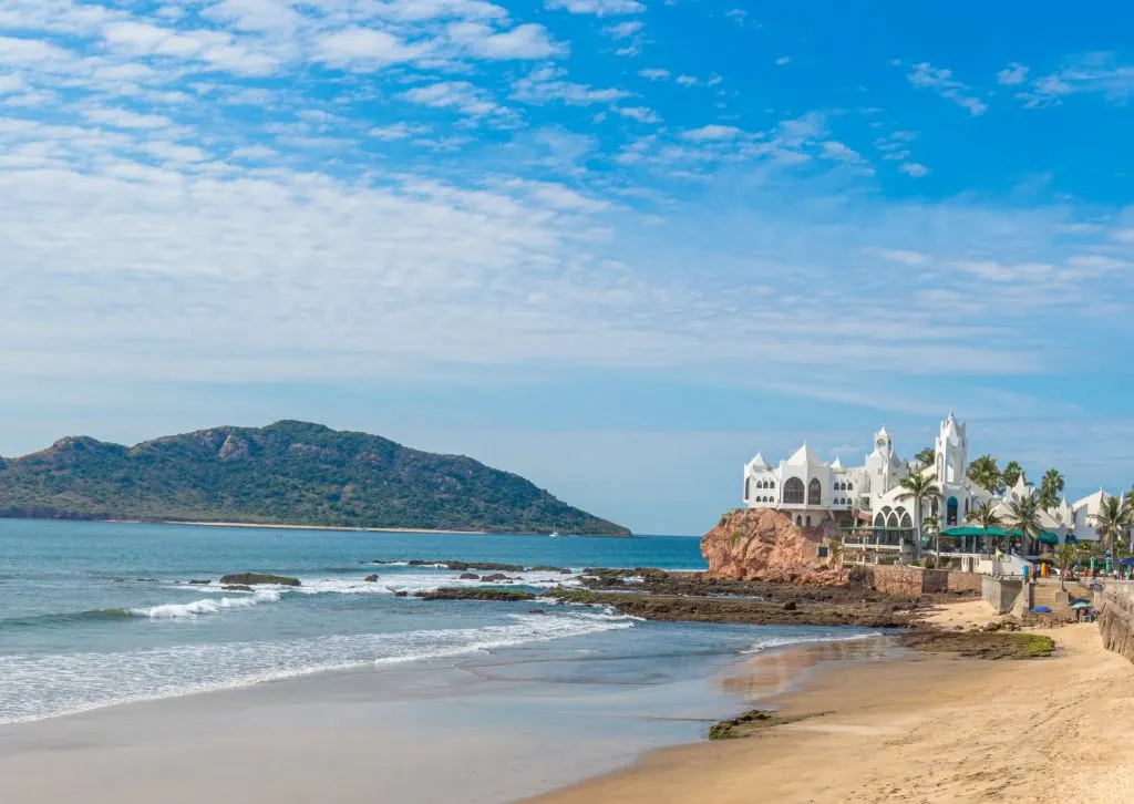 An image of the beach and the sea, with a white construction in the background in Mazatlan, Mexico