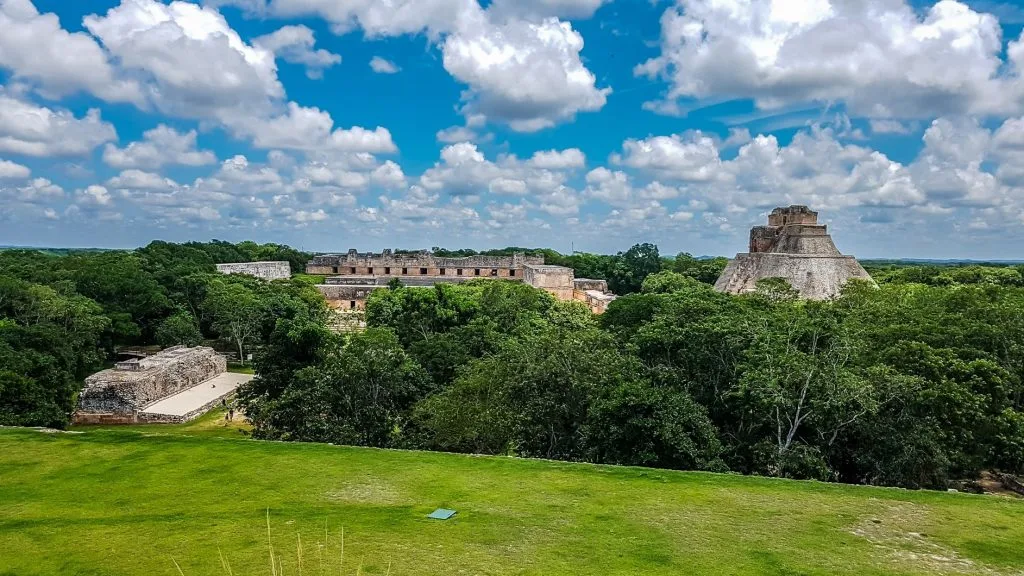 Very lush, green vegetation amidst which three Mayan structures can be seen. Image taken at Uxmal archaeological site