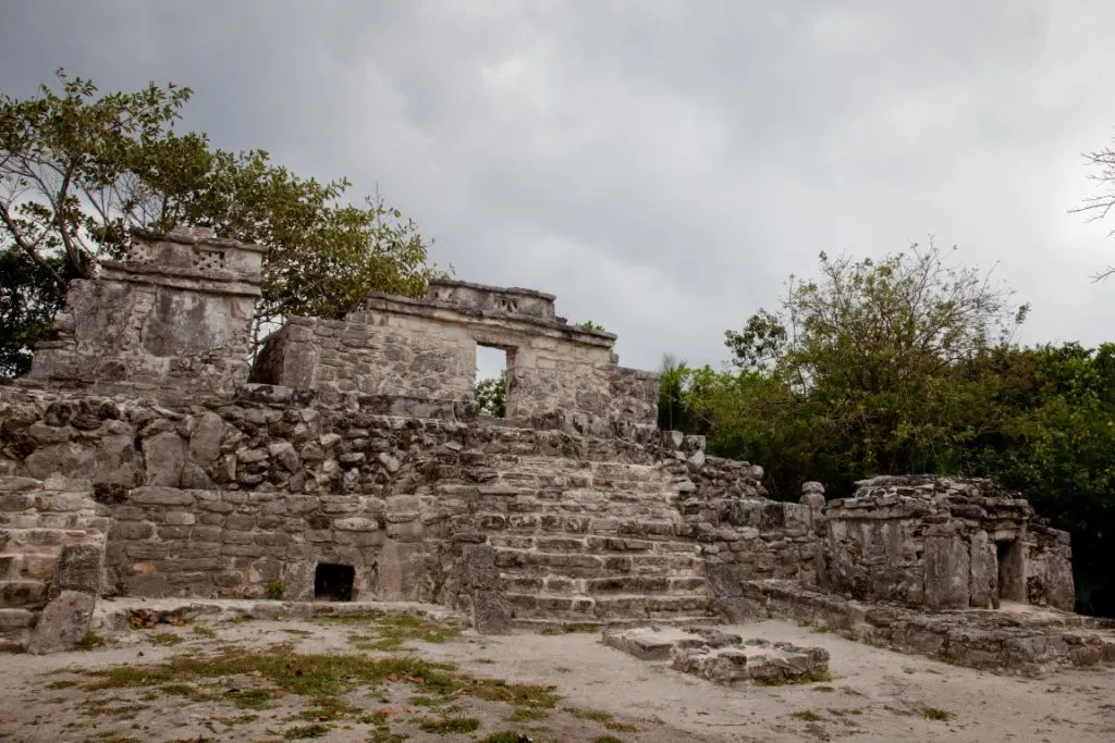 A gloomy picture of the Xcaret Ruins, with a cloudy sky and some vegetation in the background