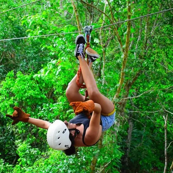 A girl hanging from a zipline with her head down, surrounded by lush greenery. Image inserted in a post about Cancun adventure parks