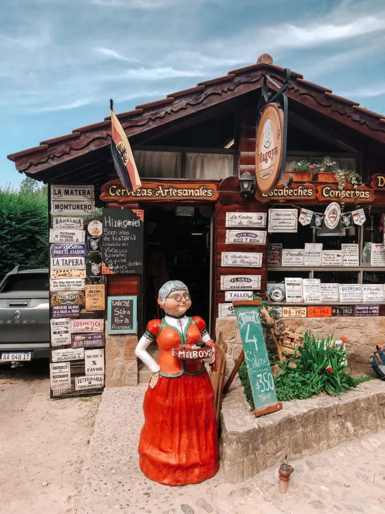 A sculpture of an old lady with an orange dress outside of a cute-looking shop 