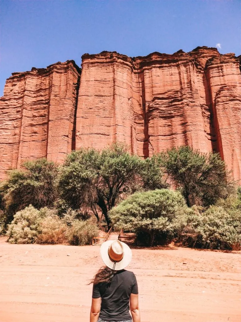 A woman looking up to a massive red rock wall 