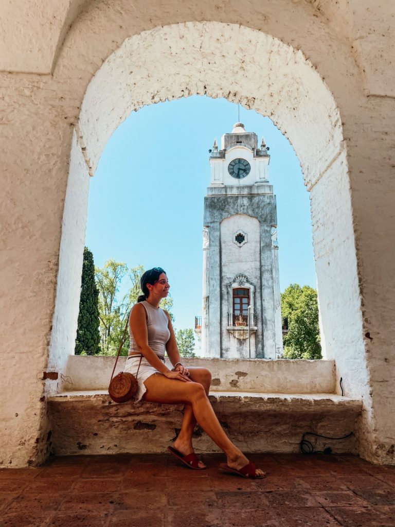 A woman sitting on a large window sill and behind her, the bell tower of a church 